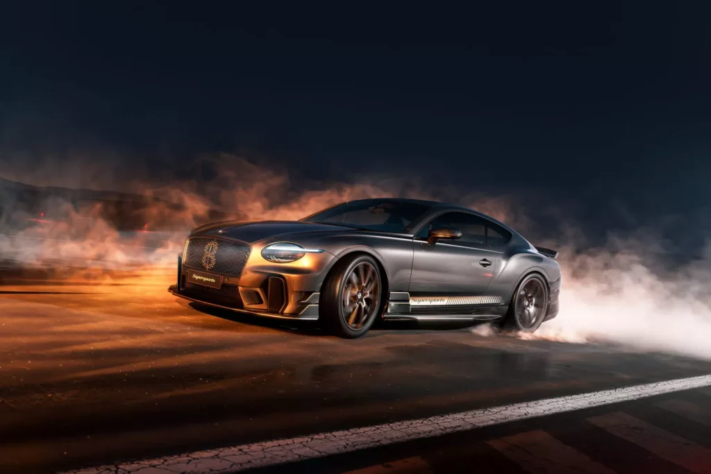 Silver luxury sports car performing a burnout at night, with flames and smoke around it on a dark road.