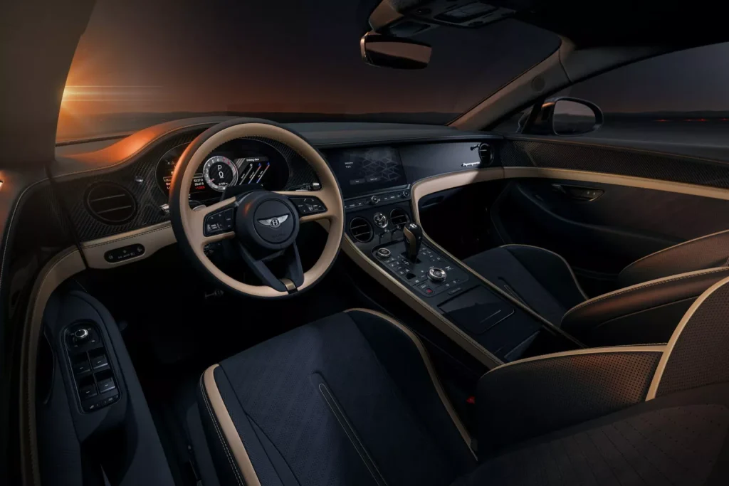 Luxurious car cabin interior with beige leather seats, dark dashboard, and sun setting outside the windshield.|Interior of a high-end car with a beige steering wheel, digital displays, and a center console at dusk
