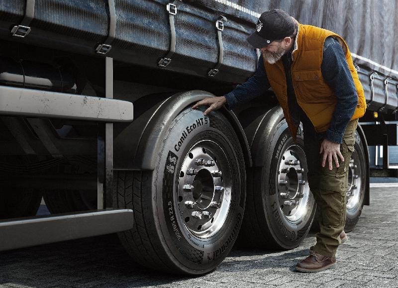Conti Eco Ht 52 | ยางรถยนต์ ราคาอัปเดต 2026 ครบทุกยี่ห้อ รวมยาง Ev | Autotirechecking Man in an orange safety vest inspecting large trailer tires beside a parked truck.