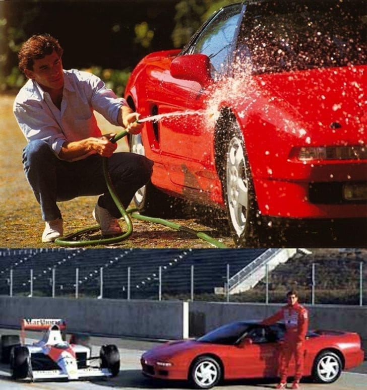 Man washing a bright red sports car with a hose in a driveway or yard, water splashing off the car's side panel.