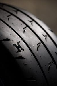 Close-up of a dark car tire showing distinctive tread grooves and wear marks.