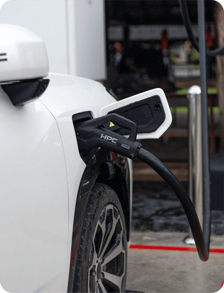 Hyperfast Charge6 | ยางรถยนต์ ราคาอัปเดต 2026 ครบทุกยี่ห้อ รวมยาง Ev | Autotirechecking Close-up of a white electric car being charged, with an HPC charging plug inserted into the car's rear port at a charging station.