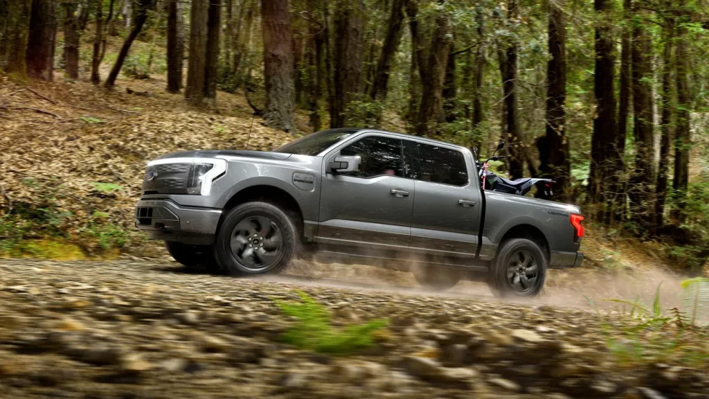 Img2987 | ยางรถยนต์ ราคาอัปเดต 2026 ครบทุกยี่ห้อ รวมยาง Ev | Autotirechecking Gray pickup truck driving fast on a dirt road through a forest, kicking up dust in the woods.