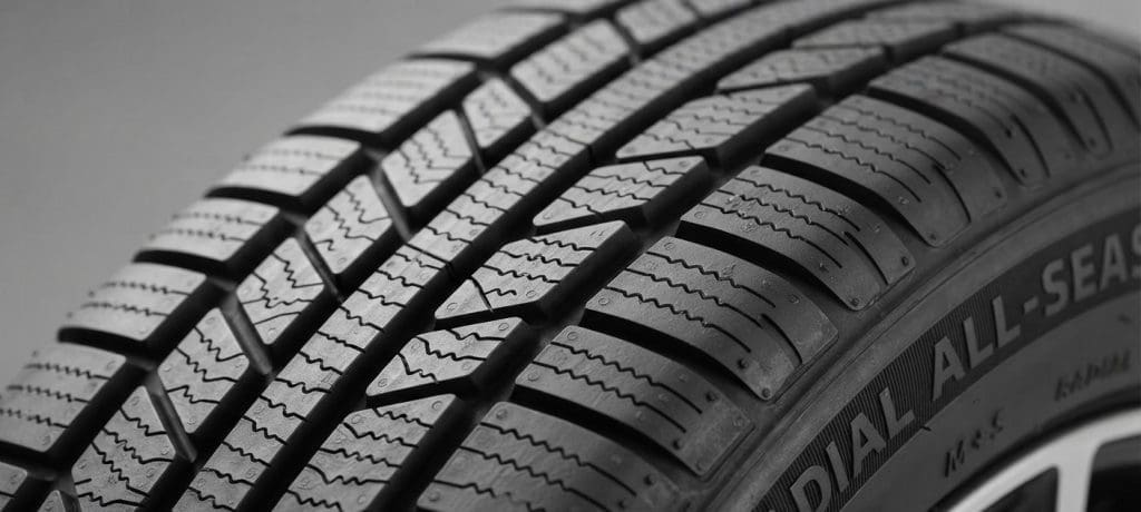 Close-up of a car tire tread showing detailed grooves and patterns with'ALL-SEASON' marking on the sidewall used to indicate tire type.