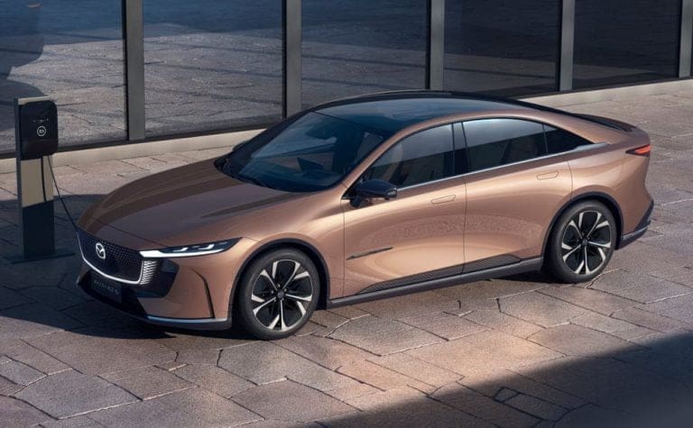 Bronze-colored Mercedes-Benz sedan parked on a paved lot beside a charging station.