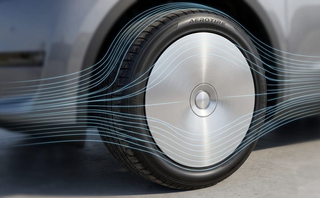 Close-up of a car wheel with a silver aerodynamic hubcap and blue airflow lines illustrating reduced air resistance around the tire.