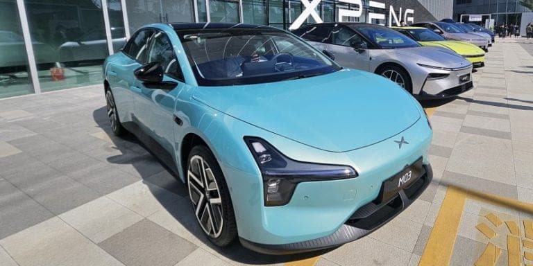 Blue XPeng M03 electric car parked outside a showroom, with other colorful cars in a row and the XPeng sign visible in the background.