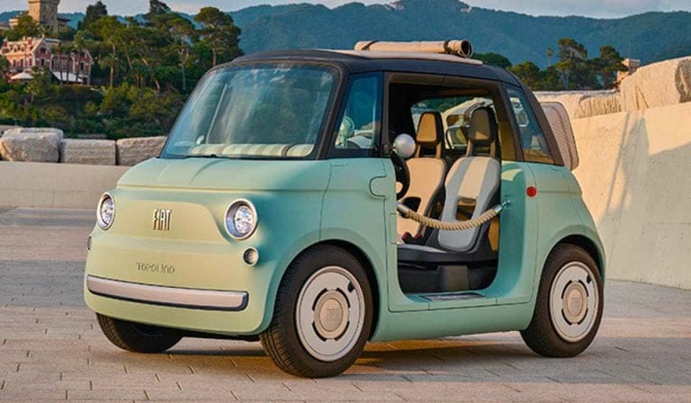 Mint green vintage Fiat 500 with the driver's door open, parked on a stone plaza with hills in the background.