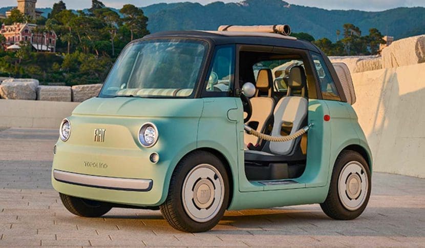 Mint green vintage Fiat 500 with the driver's door open, parked on a stone plaza with hills in the background.
