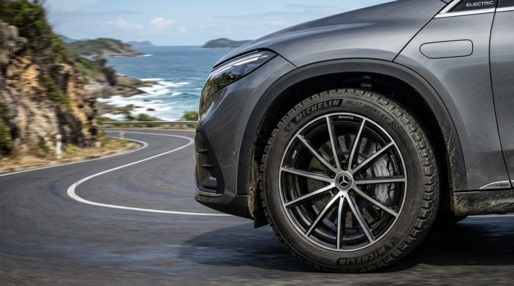 Img3346 | ยางรถยนต์ ราคาอัปเดต 2026 ครบทุกยี่ห้อ รวมยาง Ev | Autotirechecking Close-up of a gray SUV’s front right wheel on a winding coastal road, with sea and cliffs in the background.