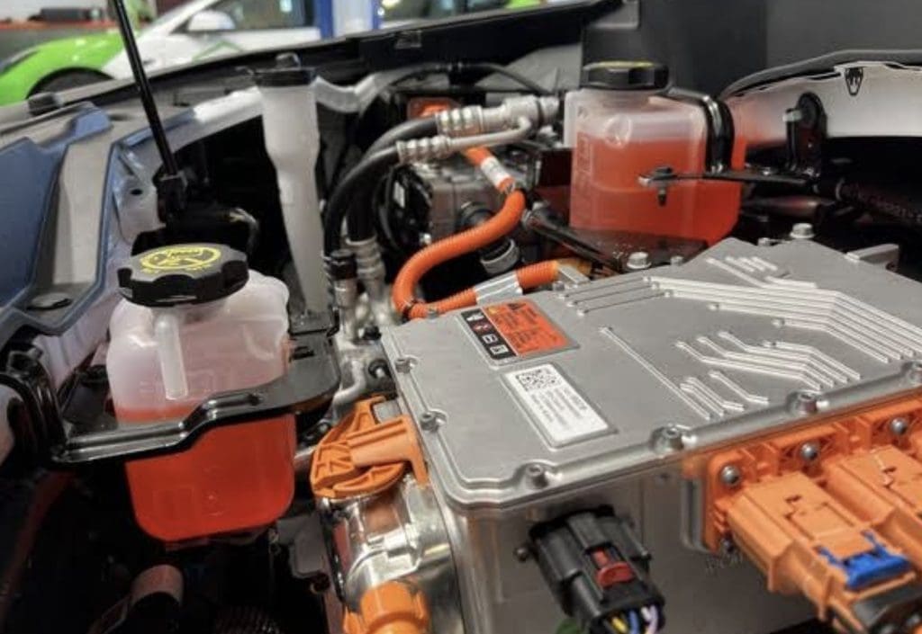 Screenshot | ยางรถยนต์ ราคาอัปเดต 2026 ครบทุกยี่ห้อ รวมยาง Ev | Autotirechecking Under-hood view of an electric vehicle powertrain: orange high-voltage cables, a metal inverter housing, and coolant and brake fluid reservoirs visible.