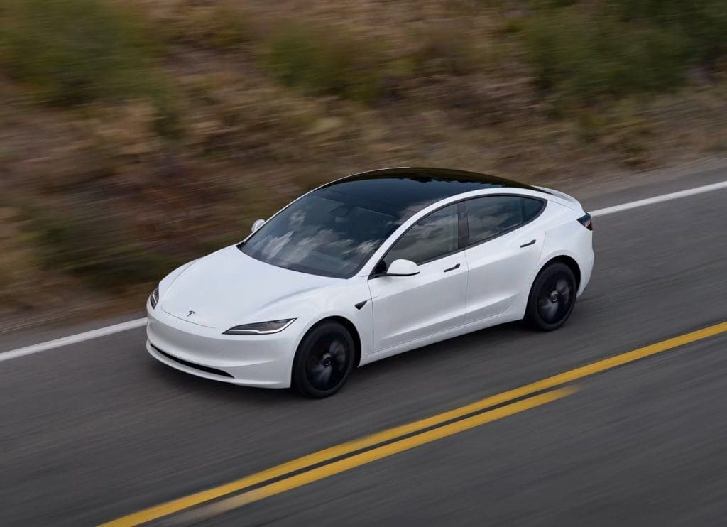 Img3604 | ยางรถยนต์ ราคาอัปเดต 2026 ครบทุกยี่ห้อ รวมยาง Ev | Autotirechecking White Tesla Model 3 sedan driving along a rural two-lane road with a blurred background, conveying speed and motion.