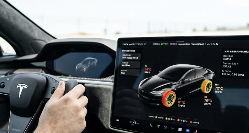 Driver's hand on the Tesla steering wheel while a large touchscreen displays a 3D car model with performance data and track info.