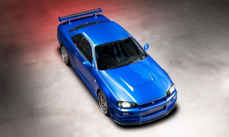 Top-down view of a vivid blue Nissan Skyline GT-R R34 sports car with a large rear spoiler in a studio lighting setup.