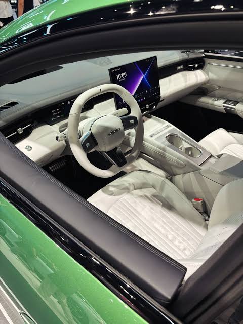 Img4441 | ยางรถยนต์ ราคาอัปเดต 2026 ครบทุกยี่ห้อ รวมยาง Ev | Autotirechecking View into the driver's cockpit of a green car, featuring white leather seats, a round steering wheel, and a large central touchscreen on the dashboard.