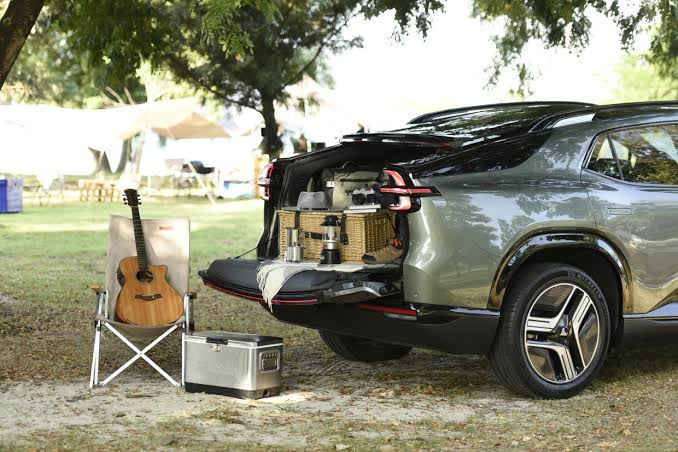 Img4452 | ยางรถยนต์ ราคาอัปเดต 2026 ครบทุกยี่ห้อ รวมยาง Ev | Autotirechecking SUV with its trunk open at a park, a guitar on a folding chair, cooler and picnic gear laid out under trees