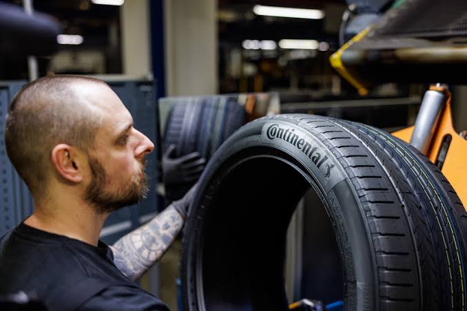 Img4662 | ยางรถยนต์ ราคาอัปเดต 2026 ครบทุกยี่ห้อ รวมยาง Ev | Autotirechecking Man with a beard inspecting a large Continental tire in an auto workshop.