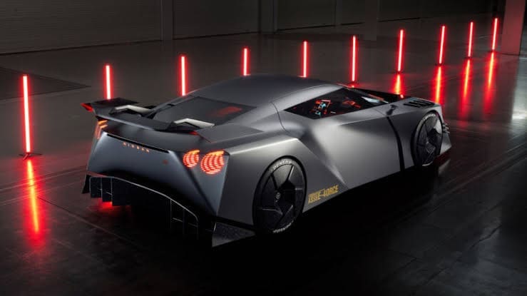 Futuristic gray concept sports car with a large rear wing and red taillights, set in a dark studio with vertical red light bars.