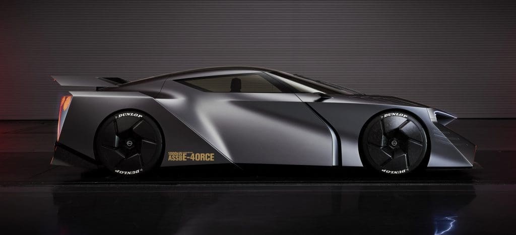 Side view of a sleek silver concept car with a low, angular profile, black Dunlop racing wheels, and a subtle rear spoiler in a studio setting.