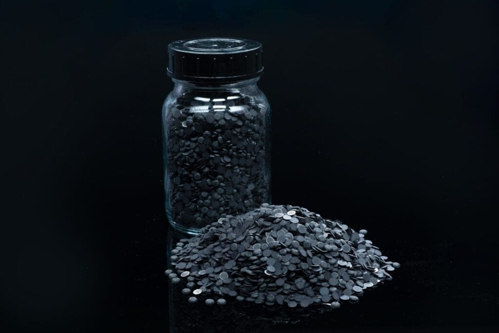 Glass jar filled with small black pellets, with many spilled in a mound on a dark surface.