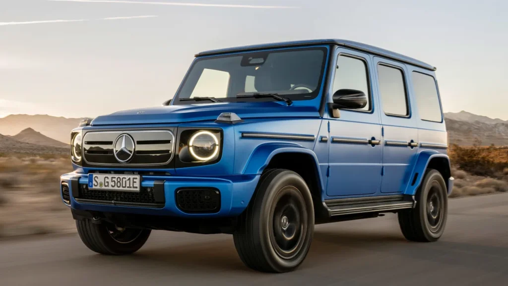 Blue Mercedes-Benz G-Class SUV driving on a desert road with mountains in the background at sunset.