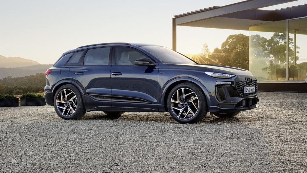 Blue SUV parked on a gravel driveway beside a modern glass-walled building at sunset, showing large alloy wheels and sleek lines.
