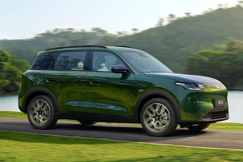 Green crossover SUV in motion on a paved road beside a lake with green hills in the background