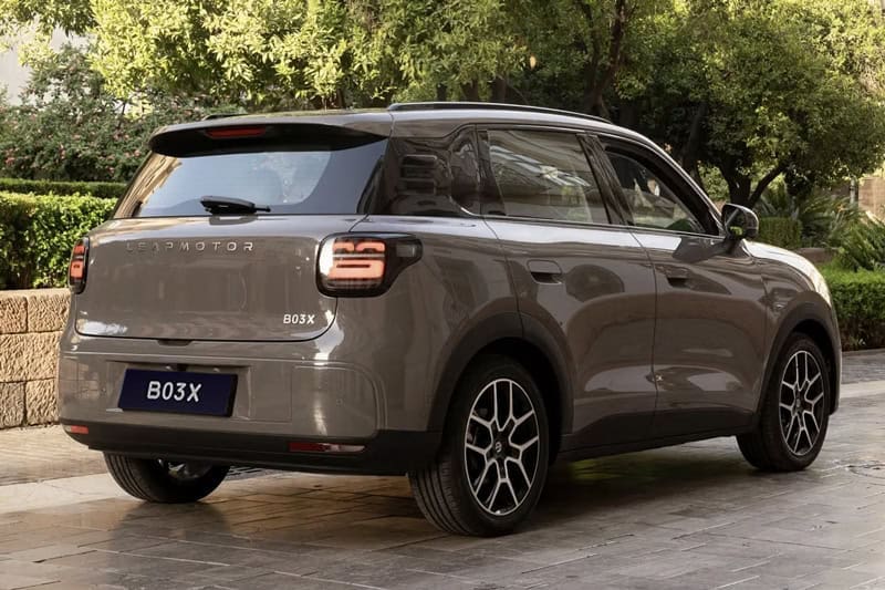 Rear three-quarter view of a gray compact SUV parked on a stone driveway, showing the back and passenger side with tinted windows and roof rails on a sunny day.