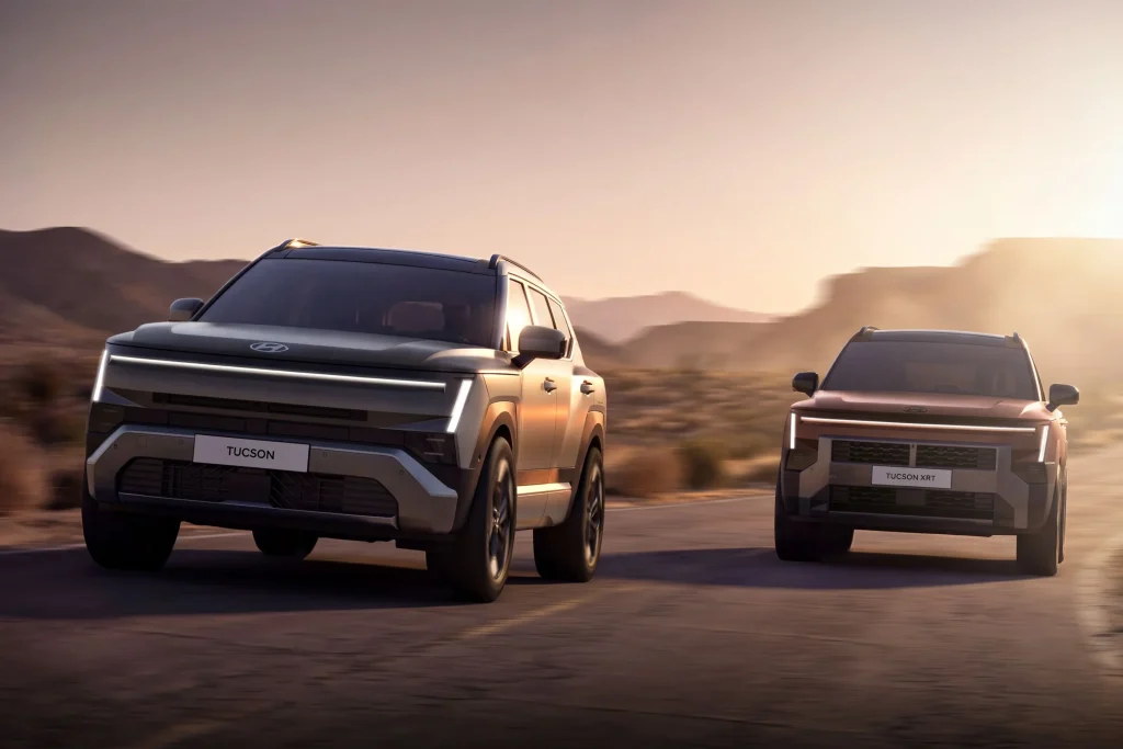 Img4868 | ยางรถยนต์ ราคาอัปเดต 2026 ครบทุกยี่ห้อ รวมยาง Ev | Autotirechecking Two Hyundai Tucson SUVs driving on a desert highway at sunset, seen from the front-right side in motion