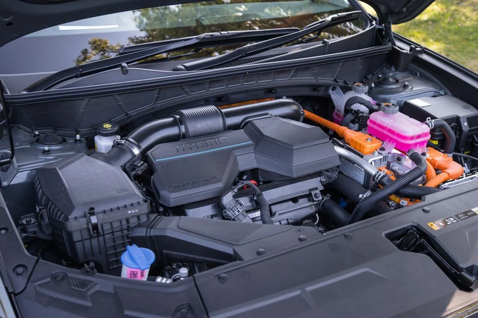 Img4869 | ยางรถยนต์ ราคาอัปเดต 2026 ครบทุกยี่ห้อ รวมยาง Ev | Autotirechecking Hybrid car engine bay with bold 'HYBRID' cover, orange high-voltage cables, pink coolant reservoir, and blue cap visible at front left.