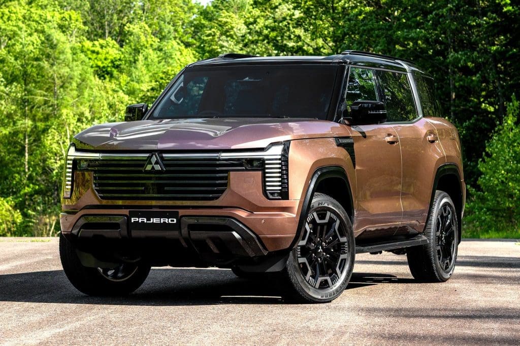 Bronze Mitsubishi Pajero SUV parked on a paved road with a green forest backdrop.