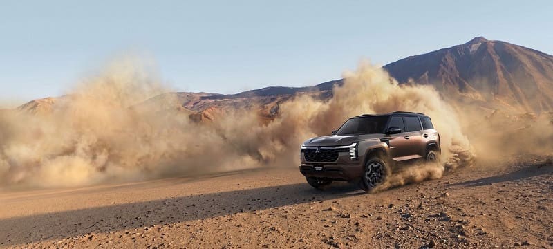 SUV kicking up dust as it drives across a barren desert with rocky hills in the distance