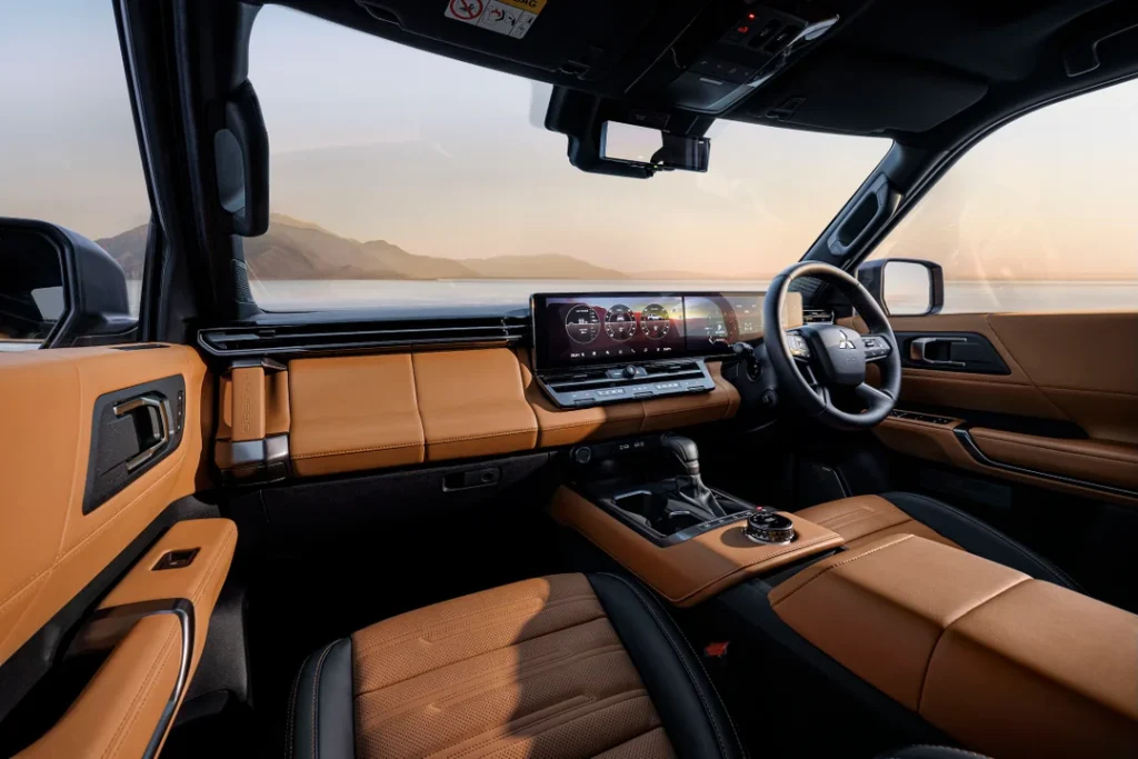 Luxurious car interior with tan leather seats, a wide digital dashboard, and a center console in a modern cockpit overlooking a desert landscape at sunset