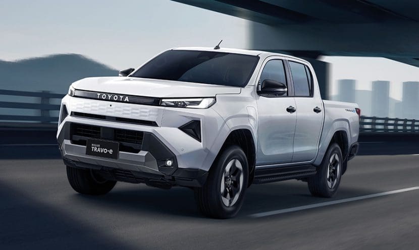 Img4885 | ยางรถยนต์ ราคาอัปเดต 2026 ครบทุกยี่ห้อ รวมยาง Ev | Autotirechecking White Toyota pickup truck driving along a highway, front three-quarter view with city skyline in the background.