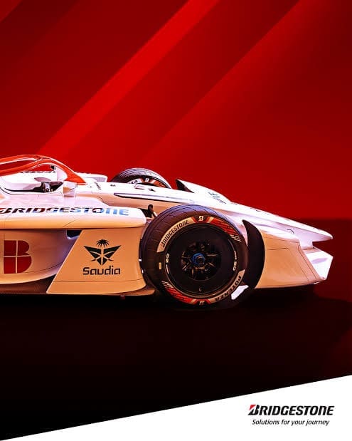 Img5032 | ยางรถยนต์ ราคาอัปเดต 2026 ครบทุกยี่ห้อ รวมยาง Ev | Autotirechecking White race car with Bridgestone branding and Saudia logo, exposed front wheel, against a red backdrop; Bridgestone logo appears bottom-right.