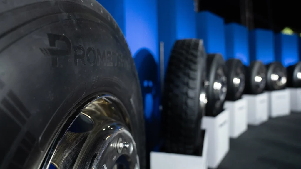 Img5058 | ยางรถยนต์ ราคาอัปเดต 2026 ครบทุกยี่ห้อ รวมยาง Ev | Autotirechecking Close-up of large black tires stacked in a row against blue walls in a showroom or workshop setting, highlighting tread and metal rims in the foreground.