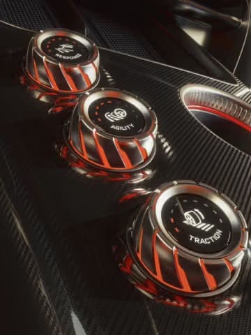 Closeup of Three Metallic Drivemode | ยางรถยนต์ ราคาอัปเดต 2026 ครบทุกยี่ห้อ รวมยาง Ev | Autotirechecking Close-up of three metallic drive-mode knobs with orange accents in a carbon-fiber car interior, one labeled Traction, indicating performance settings.