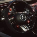 Img5143 | ยางรถยนต์ ราคาอัปเดต 2026 ครบทุกยี่ห้อ รวมยาง Ev | Autotirechecking Close-up of a Mercedes-Benz steering wheel inside a dark luxury car, with digital instrument cluster visible behind it from the cockpit perspective.