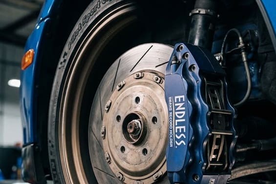 Close-up of a blue Endless brake caliper and silver rotor on a blue sports car in a workshop setting.