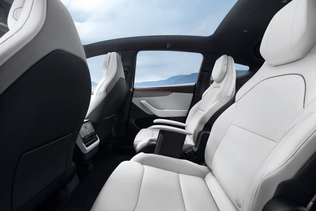 Interior of a white-leather luxury car with captain chairs, center console, and panoramic sunroof; mountains visible through the windows.