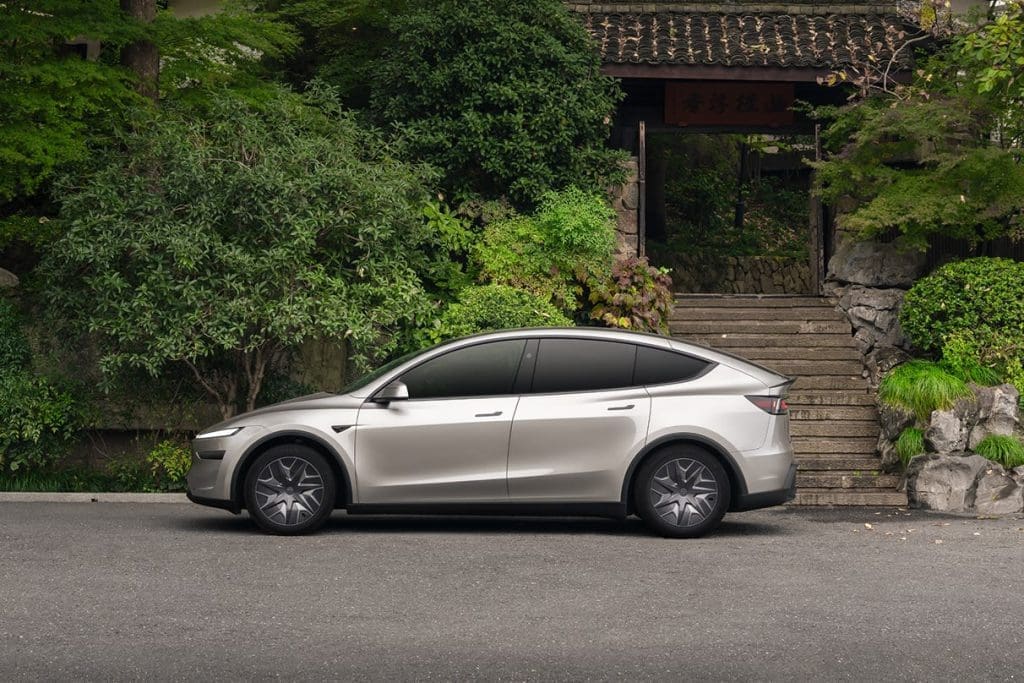 Tesla Model Yyy5 | ยางรถยนต์ ราคาอัปเดต 2026 ครบทุกยี่ห้อ รวมยาง Ev | Autotirechecking Silver sedan parked on a street in front of a stone staircase and lush greenery, with a wooden gate in the background.