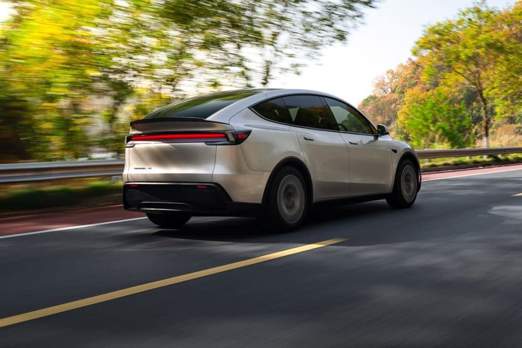 Rear three-quarter view of a silver electric car driving on a tree-lined road during daytime (fall foliage).