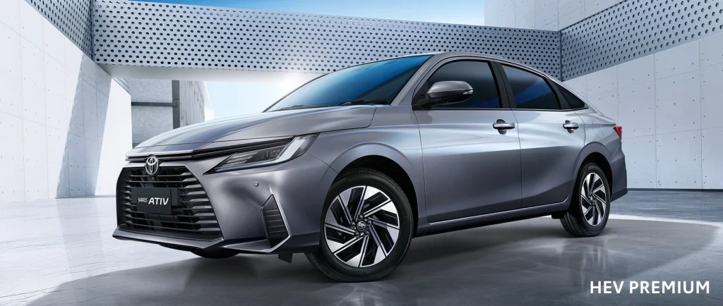 Front three-quarter view of a silver Toyota Yaris Ativ HEV Premium sedan in a modern concrete setting with sleek lines and alloy wheels.