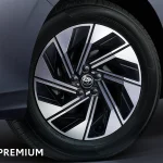 Close-up of a Toyota alloy wheel with black and silver spokes on a blue-gray car, HEV PREMIUM text visible at the bottom.