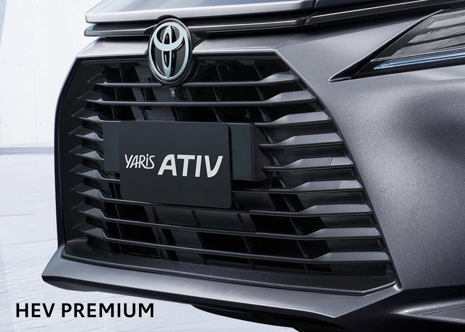 Front grille of a Toyota Yaris ATIV hybrid with Toyota emblem; plate reads YARIS ATIV, HEV PREMIUM text bottom-left.