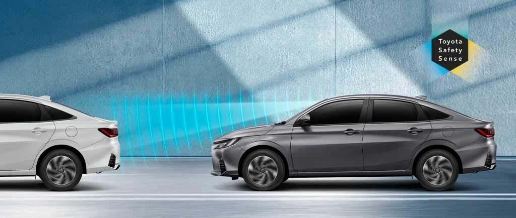 Two sedans facing each other with blue sensor-like waves between them and a Toyota Safety Sense logo on the wall behind.